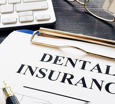 Dental insurance information on clipboard next to glasses and keyboard