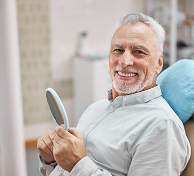 Senior man smiling while holding handheld mirror