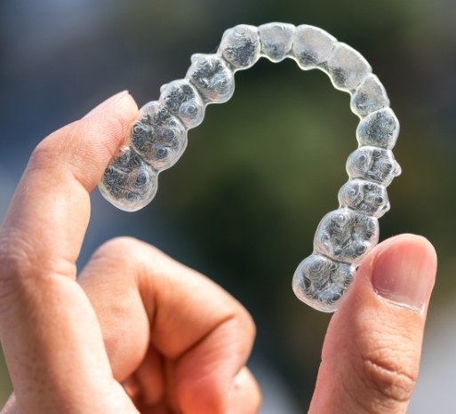 Hand holding an Invisalign clear aligner tray