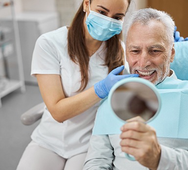 An older man admiring his new dental implants in a hand mirror