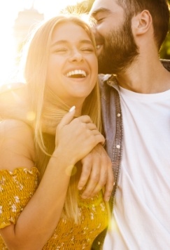 Young man hugging young woman while kissing her head outdoors