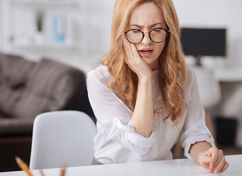 Woman with glasses and white shirt rubbing her jaw in pain