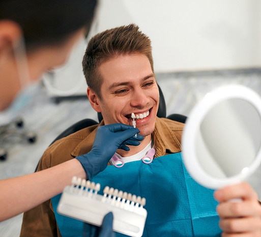 Male patient smiling while dentist selects shade of veneers